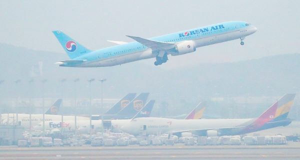 인천국제공항 주기장에 세워진 아시아나항공 여객기 위로 대한항공 여객기가 이륙하고 있다.